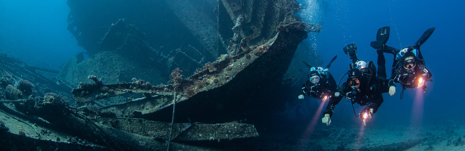 Two divers exploring a sunken shipwreck underwater.